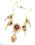 A yellow metal and red stone necklace with scrolling leaf design with pear shaped drops