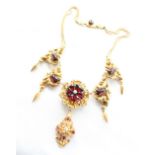 A yellow metal and red stone necklace with scrolling leaf design with pear shaped drops