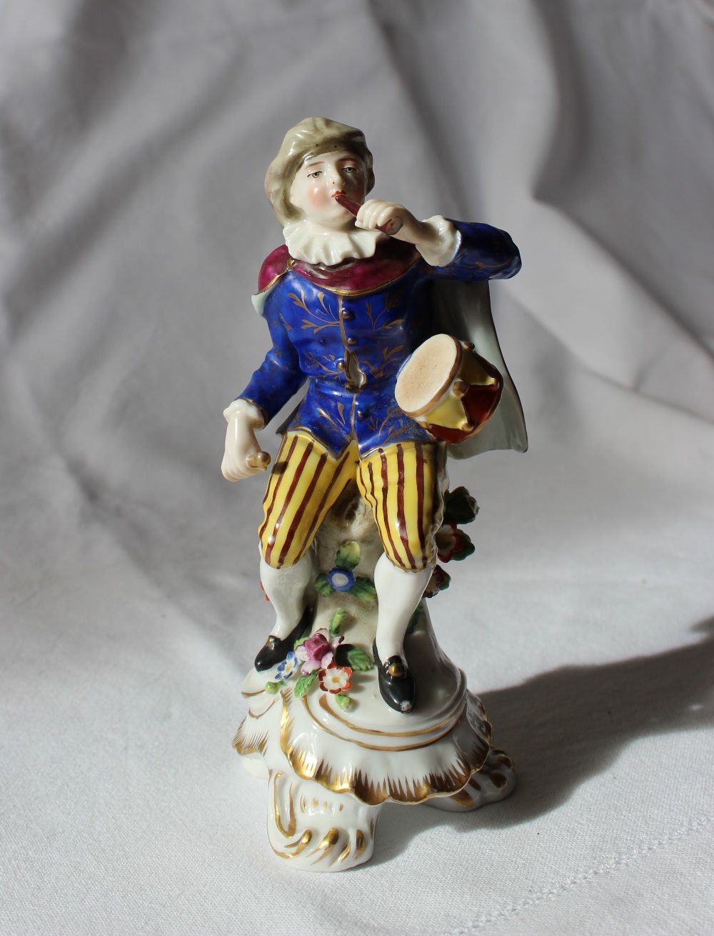 A 19th century porcelain seated figure, with a drum on his hip, in a gilt decorated blue tunic,