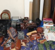 A mantle clock together with a collection of 35mm cameras, binoculars, shell cases,