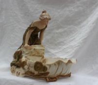 A Royal Dux pottery table centrepiece, depicting a maiden in a green dress leaning over a pond,