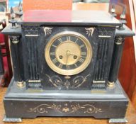 A black slate mantle clock of architectural form with a circular dial with Roman numerals