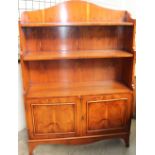 A reproduction yew waterfall bookcase with a cupboard base on bracket feet