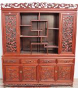 A Chinese hardwood dresser with a carved cresting, a pair of cupboard doors and shelves,