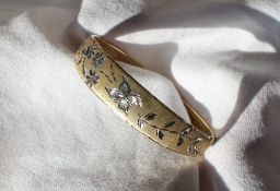 A 9ct yellow and white gold hinged bangle, decorated with flower heads and leaves, approximately 9.