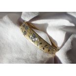 A 9ct yellow and white gold hinged bangle, decorated with flower heads and leaves, approximately 9.