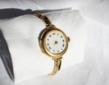 An 18ct yellow gold wristwatch with an enamel dial and Roman numerals on a yellow metal expanding