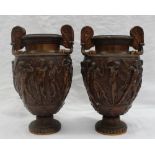 A pair of bronze twin handled urns, decorated with classical figures on a spreading foot,