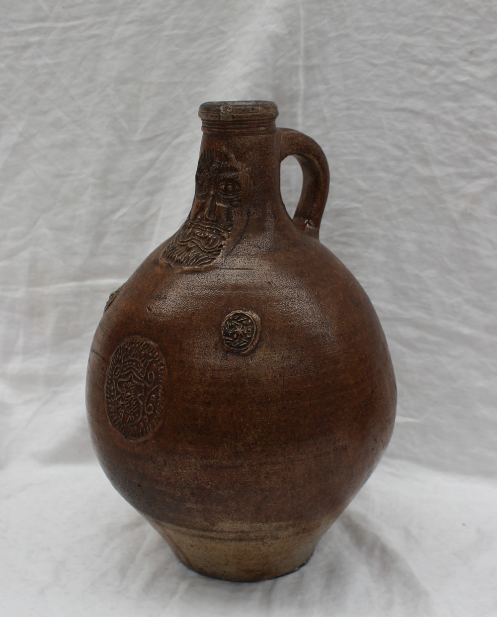 A large 18th century salt glazed Bellarmine mask jug, with a ring handle and finger marks,