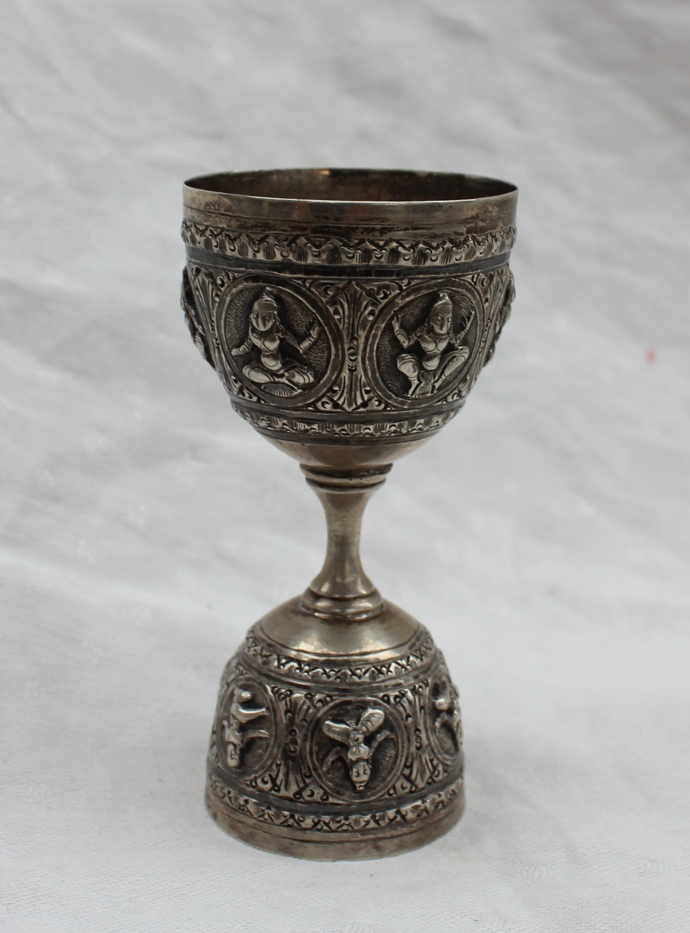 An Indian white metal double sided spirit measure, embossed with figures in roundels, 10cm high,