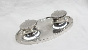 A George V silver desk standish of oval form with a raised edge and two lidded compartments with