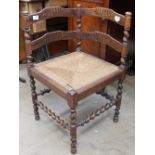 An early 20th century corner chair with ladder backs above a rush seat on turned legs united by