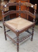 An early 20th century corner chair with ladder backs above a rush seat on turned legs united by