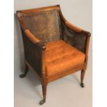 A REGENCY MAHOGANY BERGERE, the caned back, sides and seat with a padded cushion, standing on turned