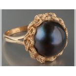 A 9CT YELLOW GOLD AND BLACK PEARL RING, pearl set in a rope form scrolled frame, on split