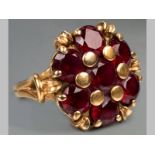A 9CT YELLOW GOLD AND GARNET RING, seven garnets claw set in floral form, ending on split shoulders,