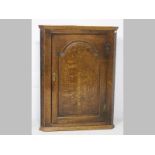 A MID-GEORGIAN OAK HANGING CORNER CABINET, the central door with an arched cushion panel door