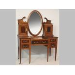 AN EDWARDIAN MAHOGANY DRESSING TABLE, the oval mirror flanked by a broken arch and small cupboards