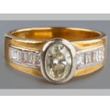 AN 18CT YELLOW GOLD DIAMOND RING, oval rube set diamond, flanked by three channel set baguettes,