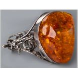 AN AMBER AND SILVER BANGLE, centre set with large organic form amber, hinged bangle decorated with