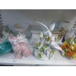 A shelf of decorative ceramics, including an Italian group of parakeets, two seated cats, two Kaiser