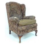 A mid 20th century wing armchair, with rollover arms and cabriole front legs,