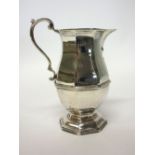 A silver milk jug of octagonal baluster form, with a scrolling handle, raised on an octagonal foot,