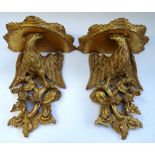 A pair of gilt framed wall brackets cast as a pair of opposing eagles, on foliate bases,