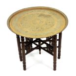 An Indian brass tray table, late 19th century, embossed with foliate filled panels,
