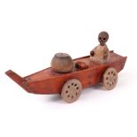 A carved wooden Japanese Kobi toy of a deathly figure on a wheeled boat, sat opposite a basket,