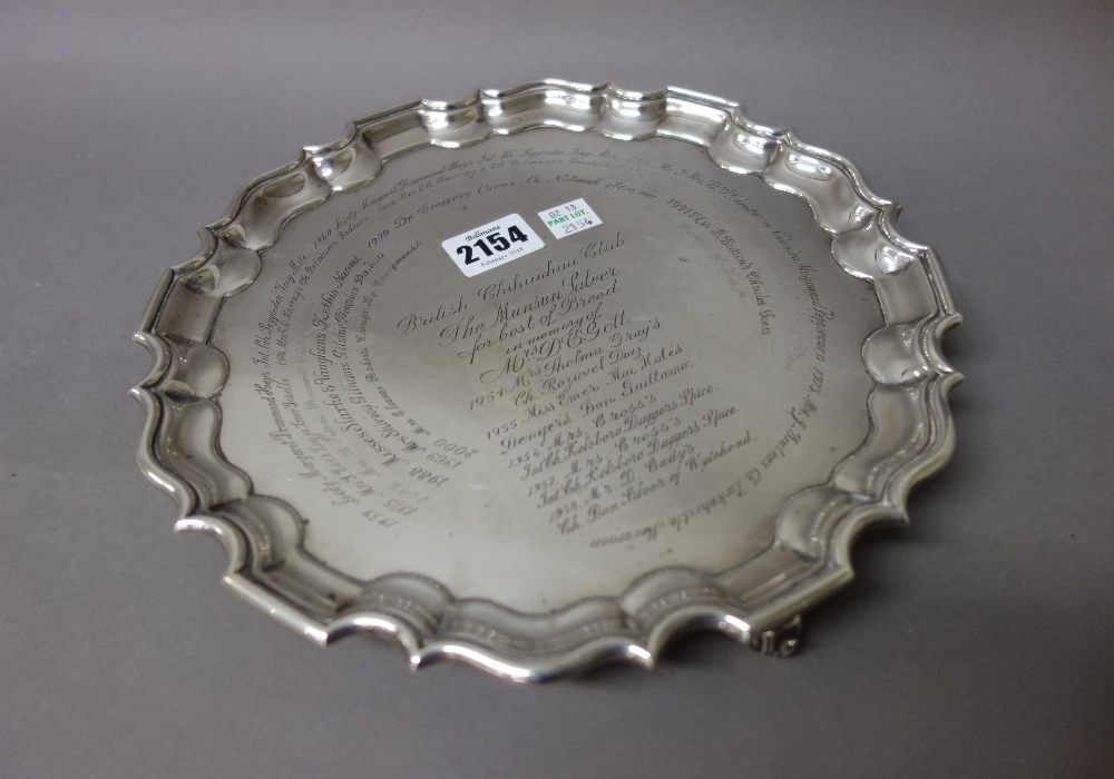 A silver salver of shaped circular form, having a pie crust rim raised on three scrolled feet,