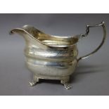 A late George III Irish silver milk jug, having a decorated rim, raised on four paw feet,