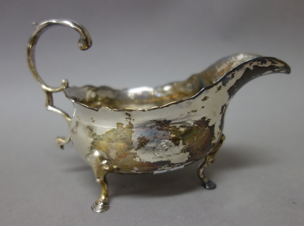 A George III silver sauceboat, with a scrolling handle, shaped rim and raised on three pad feet,