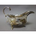 A George III silver sauceboat, with a scrolling handle, shaped rim and raised on three pad feet,