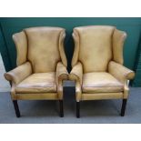 A pair of George II style leather upholstered wingback armchairs, on channelled square supports,