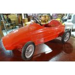 An early 20th century red painted metal Maserati pedal car, 97cm wide.