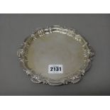 A silver shaped circular card tray, decorated with a scrolled border, raised on three bun feet,