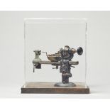 A perspex cased watchmaker's lathe 27cm. square.