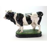 A large painted plaster figure of a standing Friesian cow, on an oval plinth base, 47cm wide,