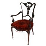 An Edwardian mahogany salon elbow chair, with a shaped foliate carved and pierced back,