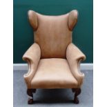 An 18th century style brown leather upholstered wingback chair, of unusual outline,