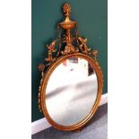 A George III style gilt framed oval mirror, with floral draped urn crest, 55cm wide x 100cm high.