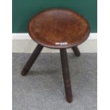 An early 19th century milking stool, the dished circular mahogany top on three turned supports,