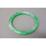 A Chinese jadeite bangle, of apple green and grey tone, 7.5cm. diameter.