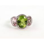 A white gold, peridot and pink tourmaline three-stone ring, within a brilliant-cut diamond surround,