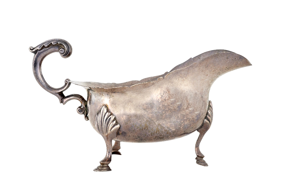 A silver sauceboat, having a shaped rim, scrolling handle and raised on three hoof shaped feet,