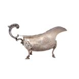 A silver sauceboat, having a shaped rim, scrolling handle and raised on three hoof shaped feet,
