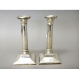 A pair of silver table candlesticks, each column raised on a square base (loaded), modern,