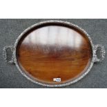 A George III mahogany oval serving tray, in a foliate chased silver plated frame,