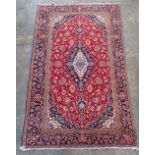 A Kashan carpet, Persian, the madder field with an elongated indigo medallion, matching spandrels,